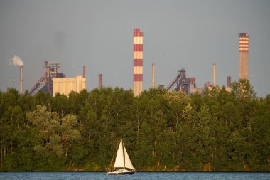Endüstriyel çelik fabrikası, demir işi. Metalürjik bitki. Çelik fabrikası. Avrupa 'da ağır sanayi. Bacalardan gelen hava kirliliği. Mavi Göl 'ün arka planında demir işçiliği. Doğa ve endüstri.