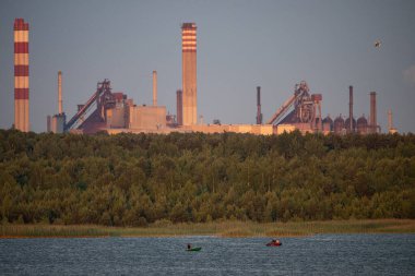 Endüstriyel çelik fabrikası, demir işi. Metalürjik bitki. Çelik fabrikası. Avrupa 'da ağır sanayi. Bacalardan gelen hava kirliliği. Mavi Göl 'ün arka planında demir işçiliği. Doğa ve endüstri.