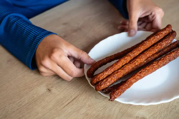 The woman holds food in her hand. The girl holds kabanos sausages on a plate. Holding sausages in hand.