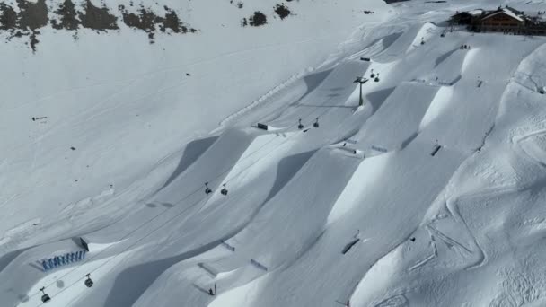 マドンナ カンペリオの空中ドローンビューとヴァレンデナ ドロマイト トレンティーノ イタリアのスノーパーク スノーボーダースキーヤーはスノーパックでキッカーにジャンプ — ストック動画