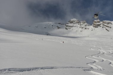 Dağlarda bir helikopter var. Kafkasya 'da serbest helikopter sörfü. Kışın serbest snowboard sporu. Helikopter paraşütü. Kar bordasında toz içinde gezmek. Kafkasya dağlarında serbest dolaşmak. 