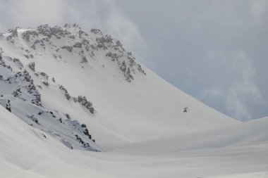 Dağlarda bir helikopter var. Kafkasya 'da serbest helikopter sörfü. Kışın serbest snowboard sporu. Helikopter paraşütü. Kar bordasında toz içinde gezmek. Kafkasya dağlarında serbest dolaşmak. 