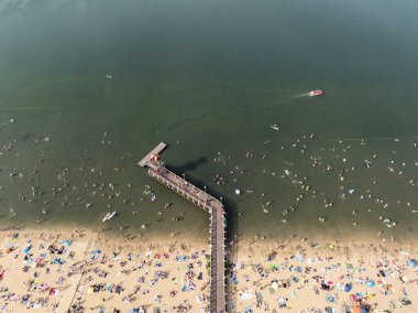 Summer Lake Sahili 'nin hava aracı görüntüsü. Yeşil gölde güneşli bir yaz tatili. Güneşlenmek ve sahilde dinlenmek. Polonya 'daki gölde tatil. İnsanlar göl sahilinde güneşleniyor..