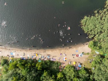Summer Lake Sahili 'nin hava aracı görüntüsü. Yeşil gölde güneşli bir yaz tatili. Güneşlenmek ve sahilde dinlenmek. Polonya 'daki gölde tatil. İnsanlar göl sahilinde güneşleniyor..