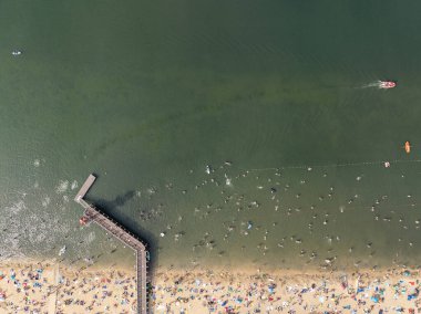 Summer Lake Sahili 'nin hava aracı görüntüsü. Yeşil gölde güneşli bir yaz tatili. Güneşlenmek ve sahilde dinlenmek. Polonya 'daki gölde tatil. İnsanlar göl sahilinde güneşleniyor..