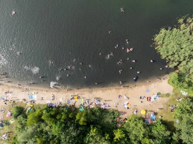 Summer Lake Sahili 'nin hava aracı görüntüsü. Yeşil gölde güneşli bir yaz tatili. Güneşlenmek ve sahilde dinlenmek. Polonya 'daki gölde tatil. İnsanlar göl sahilinde güneşleniyor..