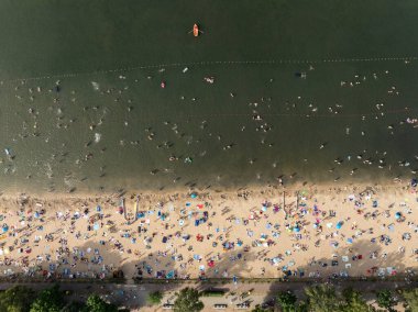 Summer Lake Sahili 'nin hava aracı görüntüsü. Yeşil gölde güneşli bir yaz tatili. Güneşlenmek ve sahilde dinlenmek. Polonya 'daki gölde tatil. İnsanlar göl sahilinde güneşleniyor..