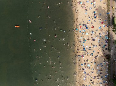 Summer Lake Sahili 'nin hava aracı görüntüsü. Yeşil gölde güneşli bir yaz tatili. Güneşlenmek ve sahilde dinlenmek. Polonya 'daki gölde tatil. İnsanlar göl sahilinde güneşleniyor..
