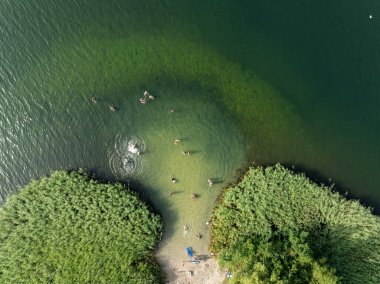 Summer Lake Sahili 'nin hava aracı görüntüsü. Yeşil gölde güneşli bir yaz tatili. Güneşlenmek ve sahilde dinlenmek. Polonya 'daki gölde tatil. İnsanlar göl sahilinde güneşleniyor..