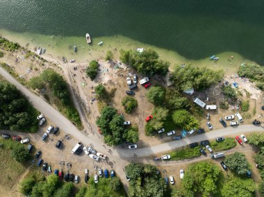 Summer Lake Sahili 'nin hava aracı görüntüsü. Yeşil gölde güneşli bir yaz tatili. Güneşlenmek ve sahilde dinlenmek. Polonya 'daki gölde tatil. İnsanlar göl sahilinde güneşleniyor..
