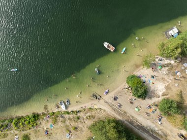 Summer Lake Sahili 'nin hava aracı görüntüsü. Yeşil gölde güneşli bir yaz tatili. Güneşlenmek ve sahilde dinlenmek. Polonya 'daki gölde tatil. İnsanlar göl sahilinde güneşleniyor..