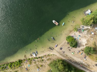 Summer Lake Sahili 'nin hava aracı görüntüsü. Yeşil gölde güneşli bir yaz tatili. Güneşlenmek ve sahilde dinlenmek. Polonya 'daki gölde tatil. İnsanlar göl sahilinde güneşleniyor..