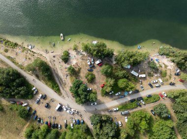 Summer Lake Sahili 'nin hava aracı görüntüsü. Yeşil gölde güneşli bir yaz tatili. Güneşlenmek ve sahilde dinlenmek. Polonya 'daki gölde tatil. İnsanlar göl sahilinde güneşleniyor..