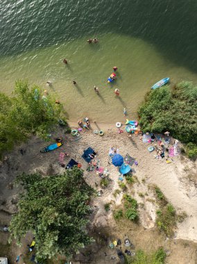 Summer Lake Sahili 'nin hava aracı görüntüsü. Yeşil gölde güneşli bir yaz tatili. Güneşlenmek ve sahilde dinlenmek. Polonya 'daki gölde tatil. İnsanlar göl sahilinde güneşleniyor..