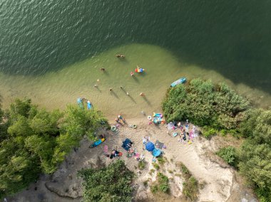 Summer Lake Sahili 'nin hava aracı görüntüsü. Yeşil gölde güneşli bir yaz tatili. Güneşlenmek ve sahilde dinlenmek. Polonya 'daki gölde tatil. İnsanlar göl sahilinde güneşleniyor..