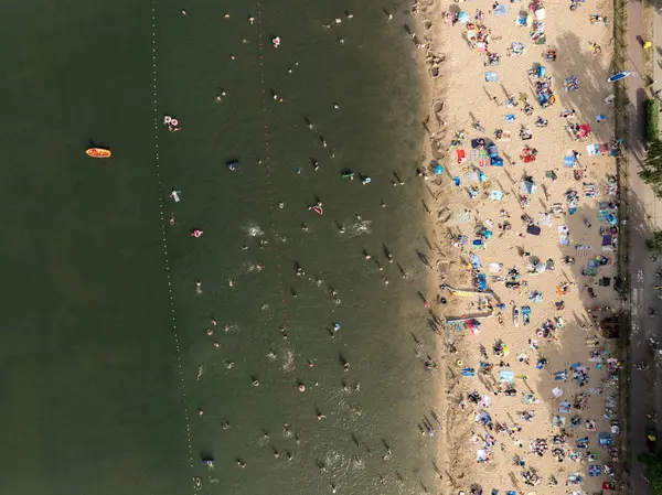 Summer Lake Sahili 'nin hava aracı görüntüsü. Yeşil gölde güneşli bir yaz tatili. Güneşlenmek ve sahilde dinlenmek. Polonya 'daki gölde tatil. İnsanlar göl sahilinde güneşleniyor..