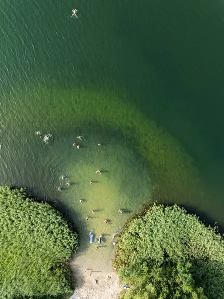 Summer Lake Sahili 'nin hava aracı görüntüsü. Yeşil gölde güneşli bir yaz tatili. Güneşlenmek ve sahilde dinlenmek. Polonya 'daki gölde tatil. İnsanlar göl sahilinde güneşleniyor..