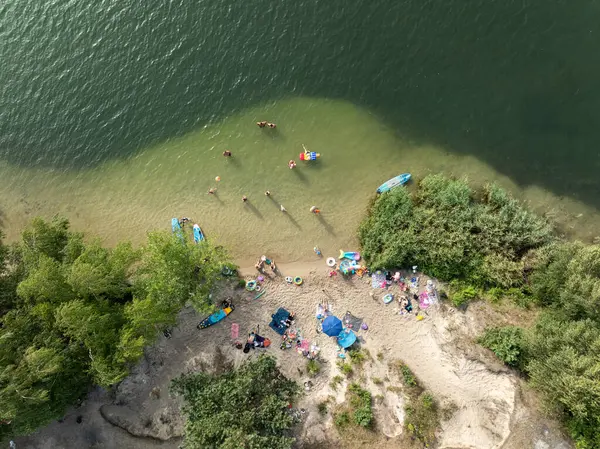 Summer Lake Sahili 'nin hava aracı görüntüsü. Yeşil gölde güneşli bir yaz tatili. Güneşlenmek ve sahilde dinlenmek. Polonya 'daki gölde tatil. İnsanlar göl sahilinde güneşleniyor..