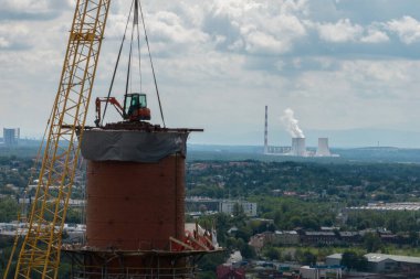 Bacanın tepesinde çalış. Vinçteki askıya alınmış bir kazıcı bacayı yok ediyor. Bacanın yıkımının insansız hava aracı görüntüsü, baca bacası üzerinde çalışan kazıcı. Küçük bir kazıcı uzun bir bacayı yok ediyor..