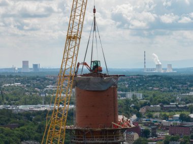 Bacanın tepesinde çalış. Vinçteki askıya alınmış bir kazıcı bacayı yok ediyor. Bacanın yıkımının insansız hava aracı görüntüsü, baca bacası üzerinde çalışan kazıcı. Küçük bir kazıcı uzun bir bacayı yok ediyor..