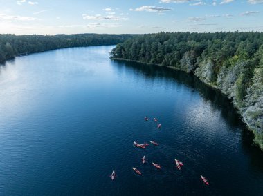 Yeşil ormanlarla çevrili bir gölde kayak yapan insanların insansız hava aracı görüntüsü. Masurian Gölü Bölgesi 'nde kırmızı kanolarla geziyorlar. Kulka Reserve 'deki Lesk Gölü, Poland.Kulka Reserve, Masuria, Polonya.