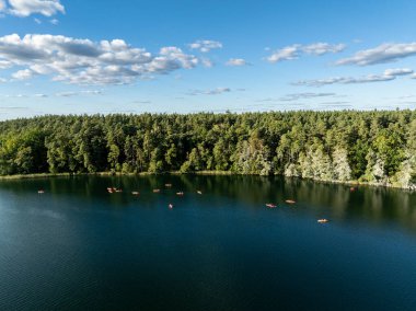 Yeşil ormanlarla çevrili bir gölde kayak yapan insanların insansız hava aracı görüntüsü. Masurian Gölü Bölgesi 'nde kırmızı kanolarla geziyorlar. Kulka Reserve 'deki Lesk Gölü, Poland.Kulka Reserve, Masuria, Polonya.