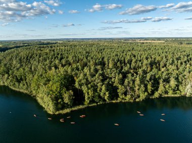 Yeşil ormanlarla çevrili bir gölde kayak yapan insanların insansız hava aracı görüntüsü. Masurian Gölü Bölgesi 'nde kırmızı kanolarla geziyorlar. Kulka Reserve 'deki Lesk Gölü, Poland.Kulka Reserve, Masuria, Polonya.