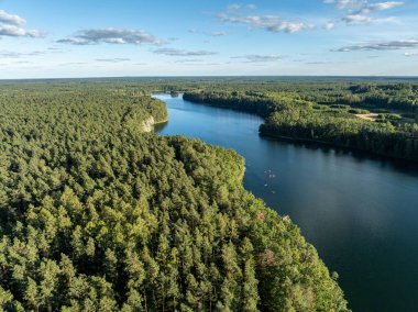 Yeşil ormanlarla çevrili bir gölde kayak yapan insanların insansız hava aracı görüntüsü. Masurian Gölü Bölgesi 'nde kırmızı kanolarla geziyorlar. Kulka Reserve 'deki Lesk Gölü, Poland.Kulka Reserve, Masuria, Polonya.
