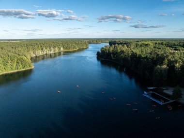 Yeşil ormanlarla çevrili bir gölde kayak yapan insanların insansız hava aracı görüntüsü. Masurian Gölü Bölgesi 'nde kırmızı kanolarla geziyorlar. Kulka Reserve 'deki Lesk Gölü, Poland.Kulka Reserve, Masuria, Polonya.