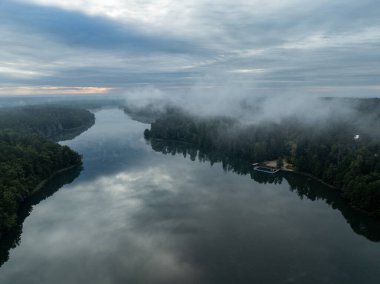Yeşil ormanla çevrili bir gölün hava aracı görüntüsü. Siste ve bulutlarda büyük bir göl. Kulka Reserve, Masuria, Polonya. Masurian Gölü bölgesinde bir göl. Polonya 'daki Kulka Reserve' de Lesk Gölü.