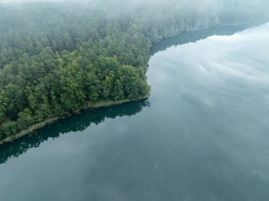 Yeşil ormanla çevrili bir gölün hava aracı görüntüsü. Siste ve bulutlarda büyük bir göl. Kulka Reserve, Masuria, Polonya. Masurian Gölü bölgesinde bir göl. Polonya 'daki Kulka Reserve' de Lesk Gölü.
