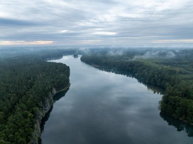Yeşil ormanla çevrili bir gölün hava aracı görüntüsü. Siste ve bulutlarda büyük bir göl. Kulka Reserve, Masuria, Polonya. Masurian Gölü bölgesinde bir göl. Polonya 'daki Kulka Reserve' de Lesk Gölü.
