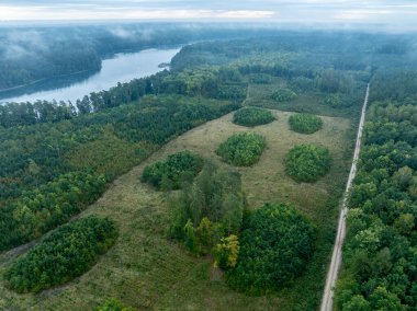 Yeşil ormanla çevrili bir gölün hava aracı görüntüsü. Siste ve bulutlarda büyük bir göl. Kulka Reserve, Masuria, Polonya. Masurian Gölü bölgesinde bir göl. Polonya 'daki Kulka Reserve' de Lesk Gölü.