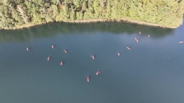 Yeşil ormanlarla çevrili bir gölde kayak yapan insanların insansız hava aracı görüntüsü. Kulka Reserve, Masuria, Polonya. Masurian Gölü Bölgesi 'nde kırmızı kanolarla geziyorlar. Polonya 'daki Kulka Reserve' de Lesk Gölü