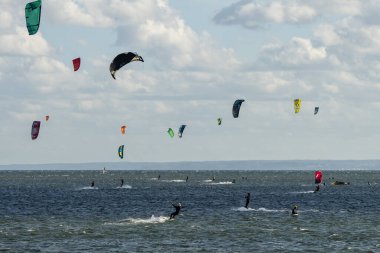 İnsanlar denizde uçurtma sörfü ya da uçurtma sörfü yapıyor. Yaz sporu uçurtma uçurmayı öğreniyor. Körfezde uçurtma sörfü dersleri. Kite sörfü. Hel Yarımadası, Puck Körfezi, Jastarnia, Polonya.