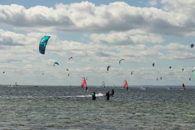 İnsanlar denizde uçurtma sörfü ya da uçurtma sörfü yapıyor. Yaz sporu uçurtma uçurmayı öğreniyor. Körfezde uçurtma sörfü dersleri. Kite sörfü. Hel Yarımadası, Puck Körfezi, Jastarnia, Polonya.