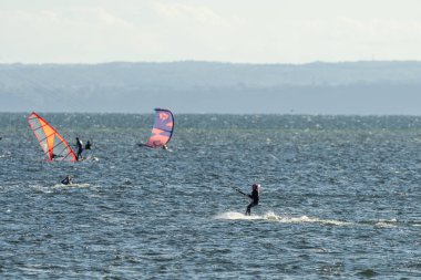 İnsanlar denizde uçurtma sörfü ya da uçurtma sörfü yapıyor. Yaz sporu uçurtma uçurmayı öğreniyor. Körfezde uçurtma sörfü dersleri. Kite sörfü. Hel Yarımadası, Puck Körfezi, Jastarnia, Polonya.
