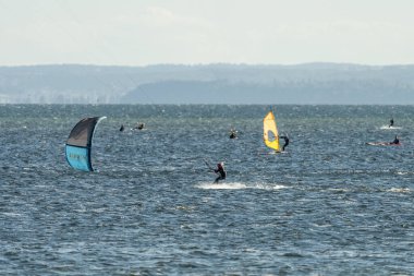 İnsanlar denizde uçurtma sörfü ya da uçurtma sörfü yapıyor. Yaz sporu uçurtma uçurmayı öğreniyor. Körfezde uçurtma sörfü dersleri. Kite sörfü. Hel Yarımadası, Puck Körfezi, Jastarnia, Polonya.