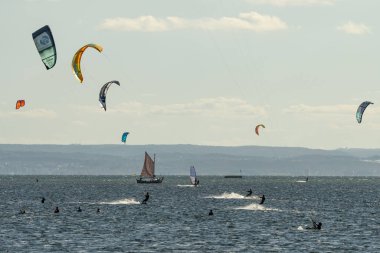 İnsanlar denizde uçurtma sörfü ya da uçurtma sörfü yapıyor. Yaz sporu uçurtma uçurmayı öğreniyor. Körfezde uçurtma sörfü dersleri. Kite sörfü. Hel Yarımadası, Puck Körfezi, Jastarnia, Polonya.