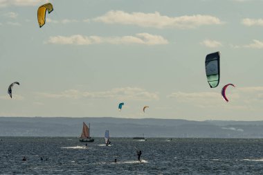 İnsanlar denizde uçurtma sörfü ya da uçurtma sörfü yapıyor. Yaz sporu uçurtma uçurmayı öğreniyor. Körfezde uçurtma sörfü dersleri. Kite sörfü. Hel Yarımadası, Puck Körfezi, Jastarnia, Polonya.