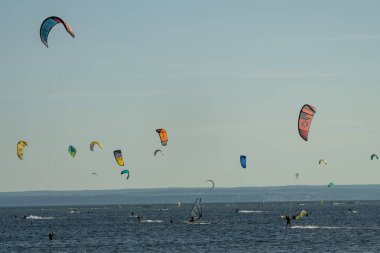 İnsanlar denizde uçurtma sörfü ya da uçurtma sörfü yapıyor. Yaz sporu uçurtma uçurmayı öğreniyor. Körfezde uçurtma sörfü dersleri. Kite sörfü. Hel Yarımadası, Puck Körfezi, Jastarnia, Polonya.