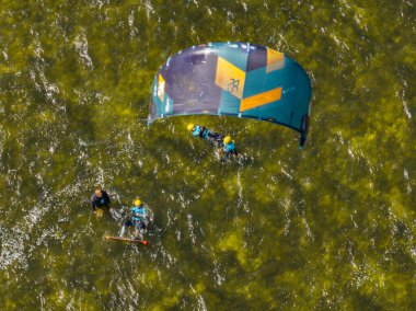 İnsanlar denizde uçurtma sörfü ya da uçurtma sörfü yapıyor. Yaz sporu uçurtma uçurmayı öğreniyor. Körfezde uçurtma sörfü dersleri. Kite sörfü. Hel Yarımadası, Puck Körfezi, Jastarnia, Polonya.