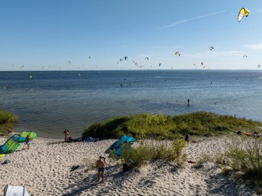 İnsanlar denizde uçurtma sörfü ya da uçurtma sörfü yapıyor. Yaz sporu uçurtma uçurmayı öğreniyor. Körfezde uçurtma sörfü dersleri. Kite sörfü. Hel Yarımadası, Puck Körfezi, Jastarnia, Polonya.
