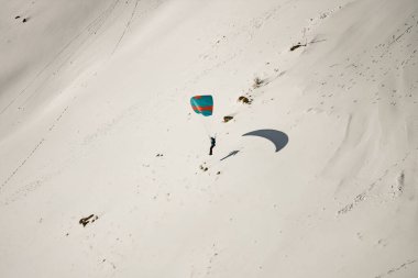 Paraglider karlı bir dağ sırasının üzerindeki bulutlarda süzülüyor. Bulutların üzerinde dramatik bir arkaplan ile paraglider. Paragliderler dağlarda karlı bir yamaçtan kalkmaya hazırlanıyorlar.