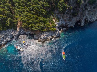 Türkiye 'nin Alanya kentindeki kayalık kıyı ve orman yakınlarındaki teknelerle turkuaz deniz manzarası. Akdeniz kıyı şeridinin ve temiz suyun insansız hava aracı görüntüleri. Alanya 'da yaz tatili