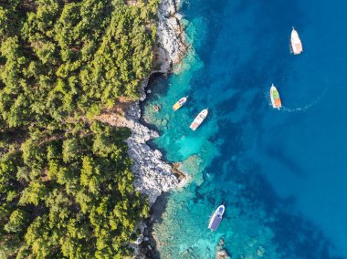 Türkiye 'nin Alanya kentindeki kayalık kıyı ve orman yakınlarındaki teknelerle turkuaz deniz manzarası. Akdeniz kıyı şeridinin ve temiz suyun insansız hava aracı görüntüleri. Alanya 'da yaz tatili