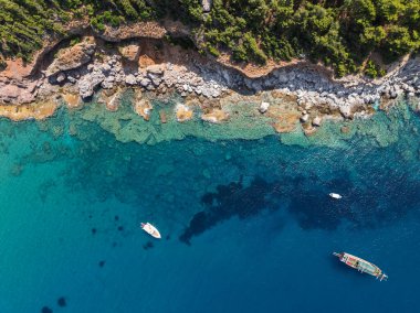 Türkiye 'nin Alanya kentindeki kayalık kıyı ve orman yakınlarındaki teknelerle turkuaz deniz manzarası. Akdeniz kıyı şeridinin ve temiz suyun insansız hava aracı görüntüleri. Alanya 'da yaz tatili