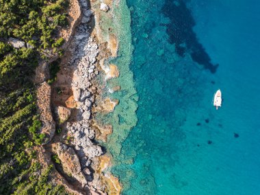 Türkiye 'nin Alanya kentindeki kayalık kıyı ve orman yakınlarındaki teknelerle turkuaz deniz manzarası. Akdeniz kıyı şeridinin ve temiz suyun insansız hava aracı görüntüleri. Alanya 'da yaz tatili