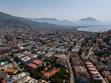 Türkiye 'deki Alanya şehrinin havadan görüntüsü. Yoğun kentsel binalar, Akdeniz kıyı şeridi, yeşil tepeler ve dağlar, açık yaz günlerinde insansız hava araçlarından. Alanya şehrindeki binaların ve otellerin havadan görüntüsü.