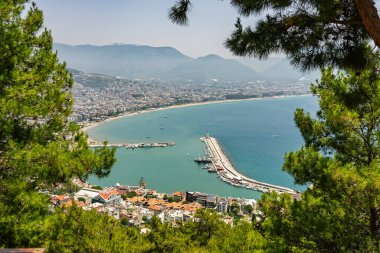 Alanya şehrinin insansız hava aracı görüntüsü, Türkiye. Sahil şeridi, Akdeniz, liman, tepenin üzerindeki tarihi şato ve açık bir yaz gününde arka planda dağların olduğu geniş kentsel alan. Alanya, Türkiye.